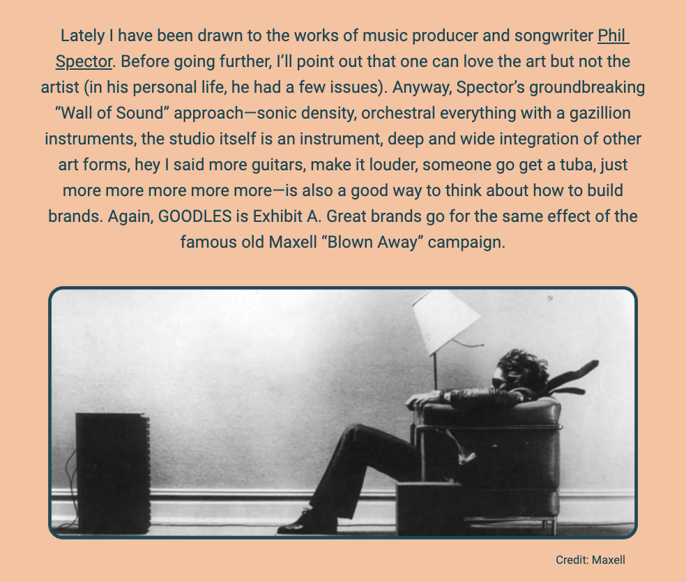The image features a monochrome photograph of a man sitting in an armchair with a high-powered speaker to his left, illustrating the intense sound force that seems to be blowing his hair and tie backward. This is a reference to the iconic Maxell "Blown Away" advertisement campaign. The scene is staged to show the power of sound, evoking the famous advertisement's message that Maxell tapes deliver a sound so clear and strong it can literally 'blow you away.'

Above the photograph is a block of text where the author expresses admiration for the work of music producer and songwriter Phil Spector, despite his personal controversies. The text highlights Spector's "Wall of Sound" technique, known for its dense orchestral aesthetic, which the author parallels with the concept of building great brands that leave a lasting impression, likening it to the impact of the Maxell campaign.

The text within the image reads:
"Lately I have been drawn to the works of music producer and songwriter Phil Spector. Before going further, I’ll point out that one can love the art but not the artist (in his personal life, he had a few issues). Anyway, Spector’s groundbreaking 'Wall of Sound' approach—sonic density, orchestral everything with a gazillion instruments, the studio itself is an instrument, deep and wide integration of other art forms, hey I said more guitars, make it louder, someone go get a tuba, just more more more more more—is also a good way to think about how to build brands. Again, GOODLES is Exhibit A. Great brands go for the same effect of the famous old Maxell 'Blown Away' campaign.

Credit: Maxell"