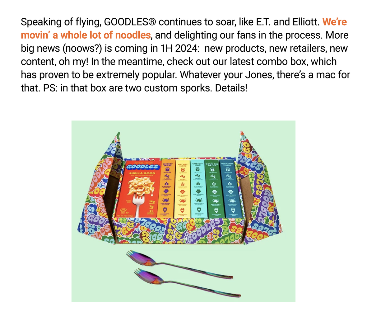 The image features a text overlay and a photo of a colorful mac and cheese product called GOODLES. The text reads: "Speaking of flying, GOODLES® continues to soar, like E.T. and Elliott. We're movin' a whole lot of noodles, and delighting our fans in the process. More big news (noows?) is coming in 1H 2024: new products, new retailers, new content, oh my! In the meantime, check out our latest combo box, which has proven to be extremely popular. Whatever your Jones, there’s a mac for that. PS: in that box are two custom sporks. Details!"

Below the text, the GOODLES mac and cheese box is opened to reveal several different flavor packets. Two customized sporks with purple and blue handles are also shown in front of the box. The background is a soft mint green.